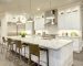 White kitchen design features large bar style kitchen island with granite countertop illuminated by modern pendant lights. Stainless steel appliances framed by white shaker cabinets . Northwest, USA